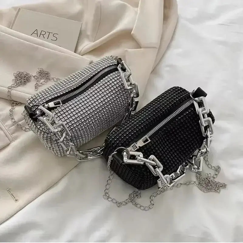 Allover rhinestone bucket bags in black and silver with chain detail on a soft fabric background.