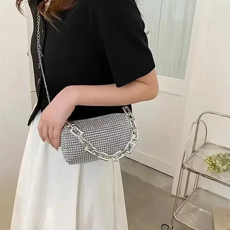 Woman carrying an allover rhinestone bucket bag with a glitter chain, styled with a chic black top and white skirt.