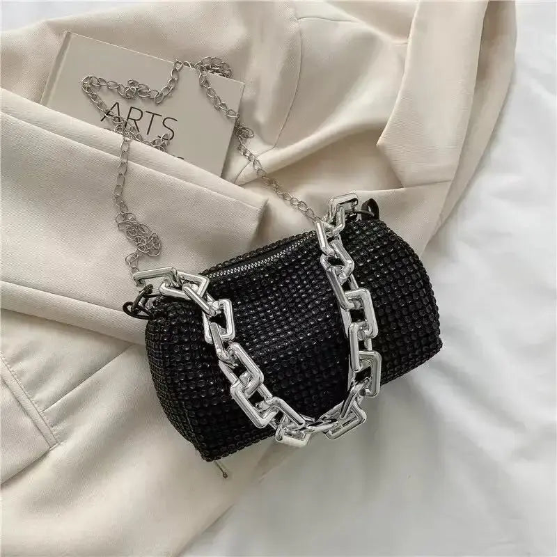 Black rhinestone bucket bag with silver chain, stylish mini crossbody purse on a light fabric background.