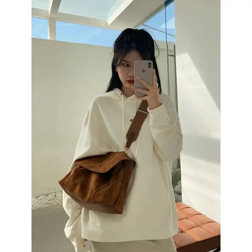 Femme portant un sac à bandoulière en cuir givré et un pull à capuche, modèle décontracté, photo en intérieur.