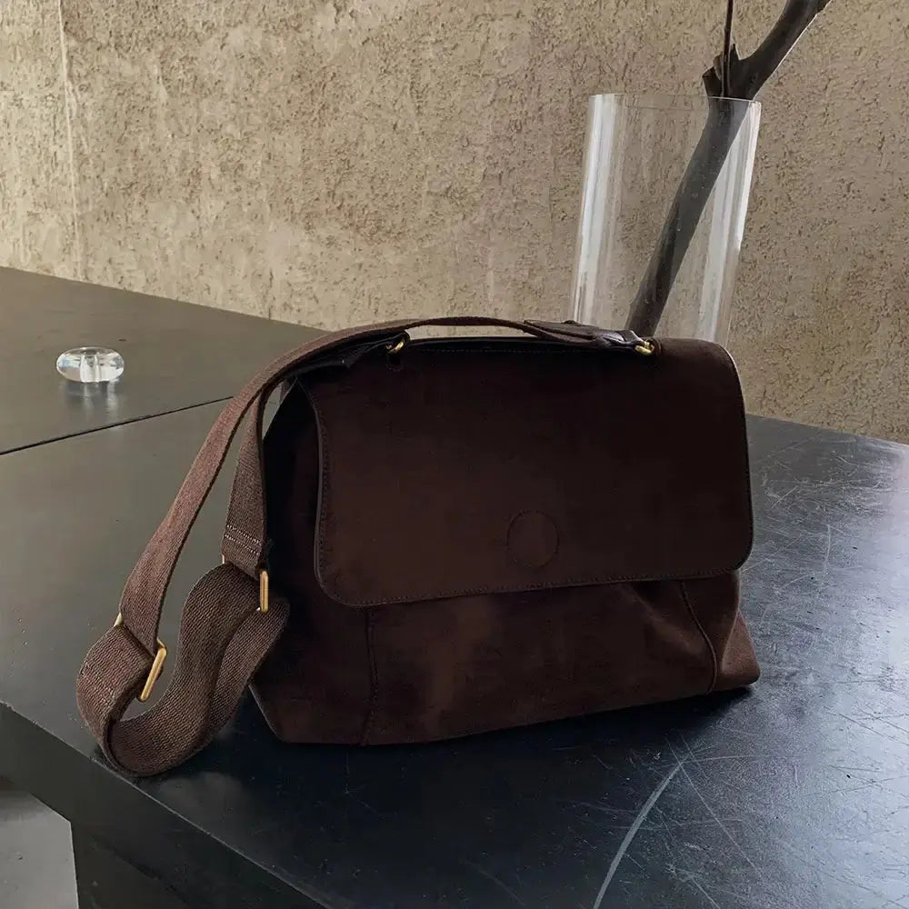 Sac à bandoulière en cuir marron, style décontracté, sur une table moderne avec vase.