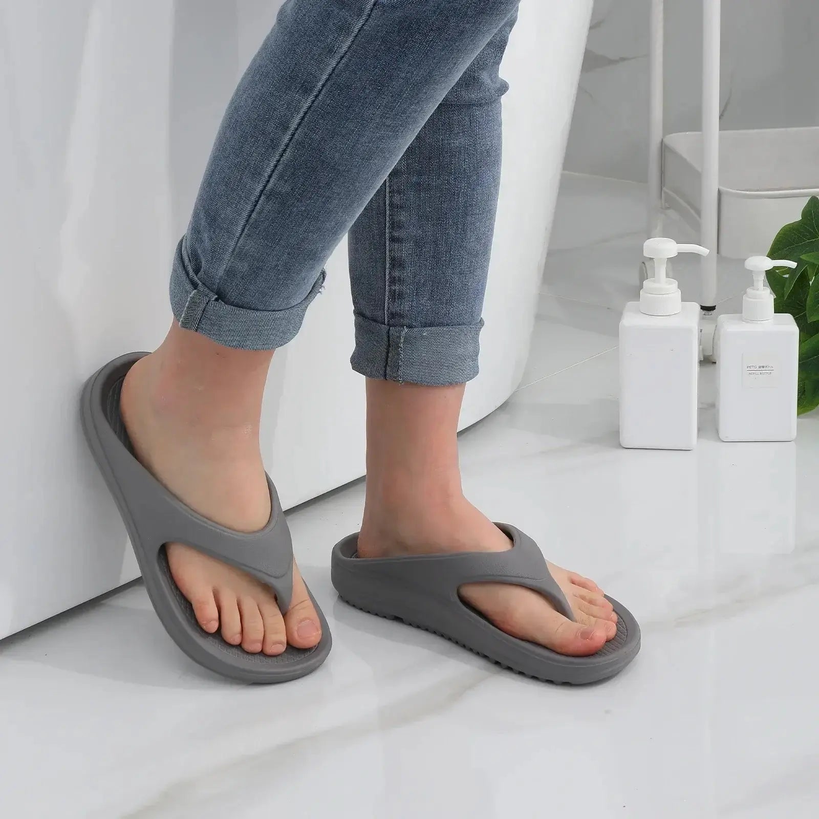 Femme portant des sandales orthopédiques grises en EVA, style moderne, confort décontracté, sur fond de salle de bain.