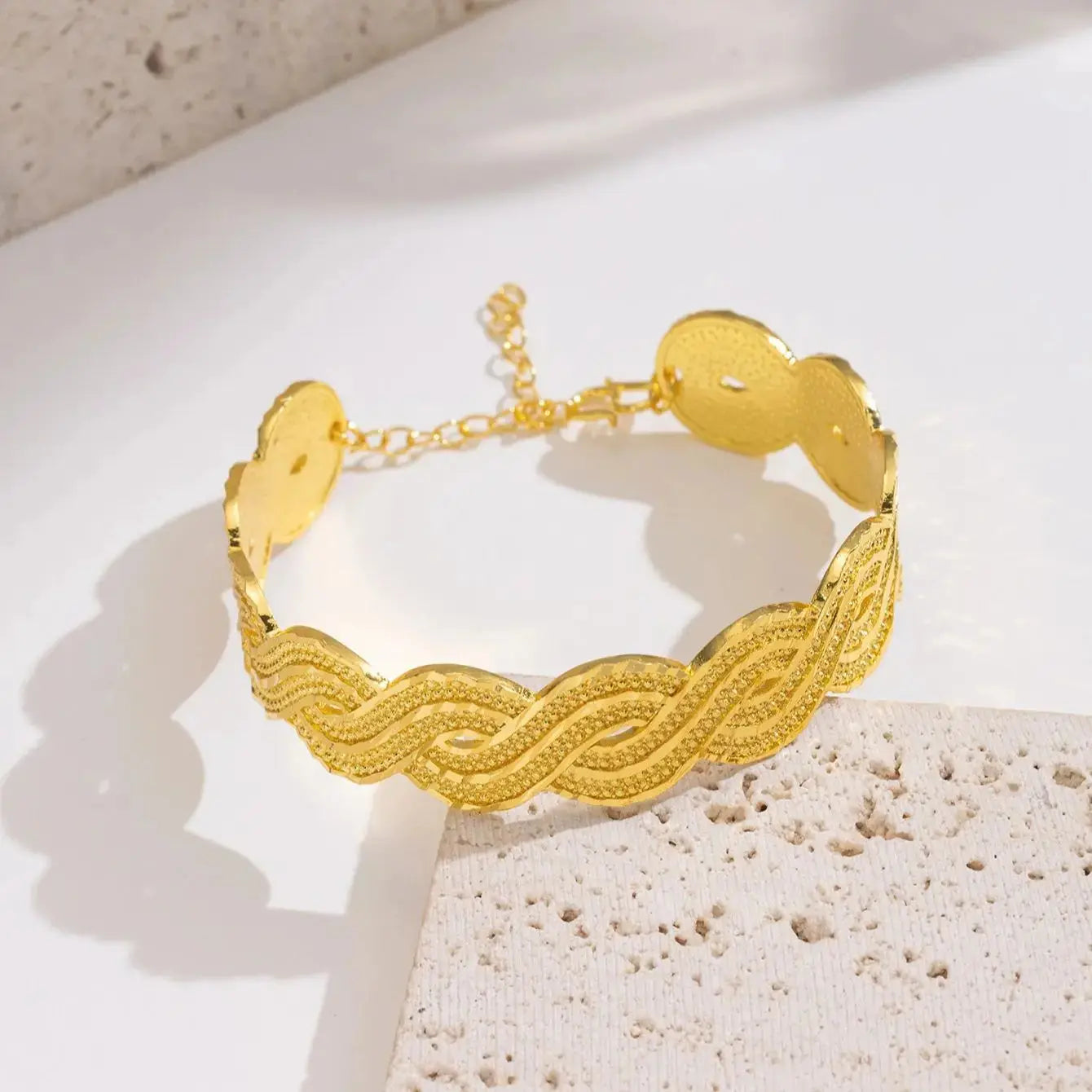 Wide gold-plated wave design cuff bracelet styled on a woman’s wrist with a traditional outfit.