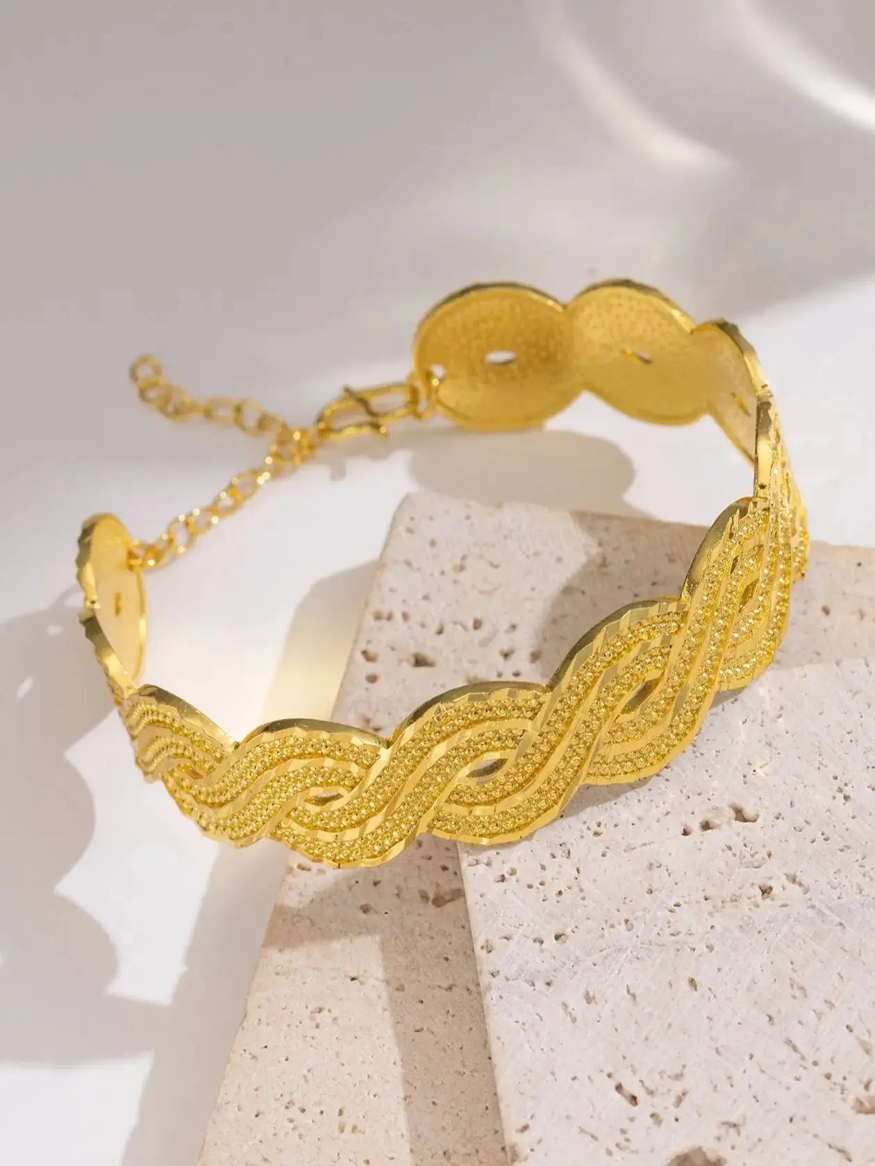 Wide gold-plated wave design cuff bracelet styled on a woman’s wrist with a traditional outfit.