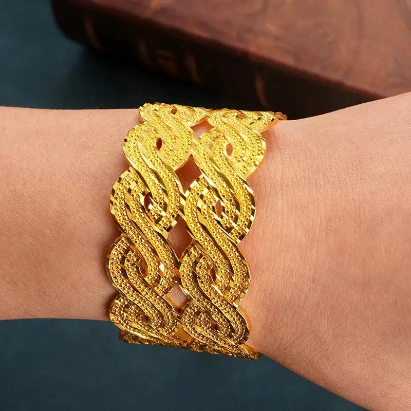 Wide gold-plated wave design cuff bracelet styled on a woman’s wrist with a traditional outfit.