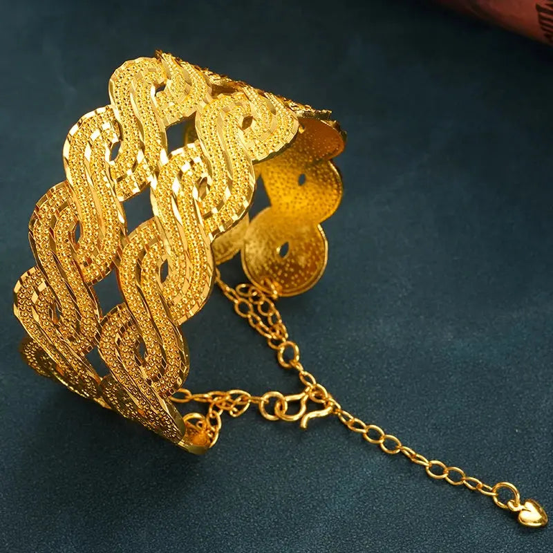 Wide gold-plated wave design cuff bracelet styled on a woman’s wrist with a traditional outfit.