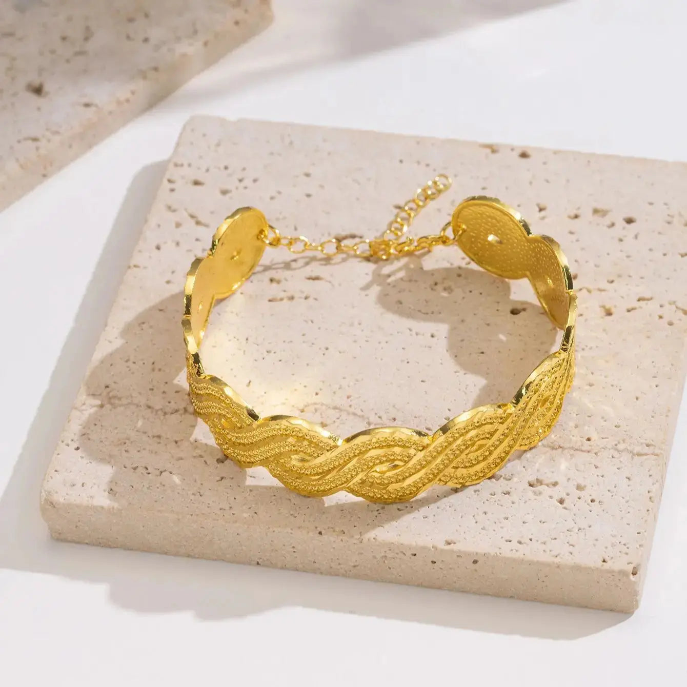 Wide gold-plated wave design cuff bracelet styled on a woman’s wrist with a traditional outfit.