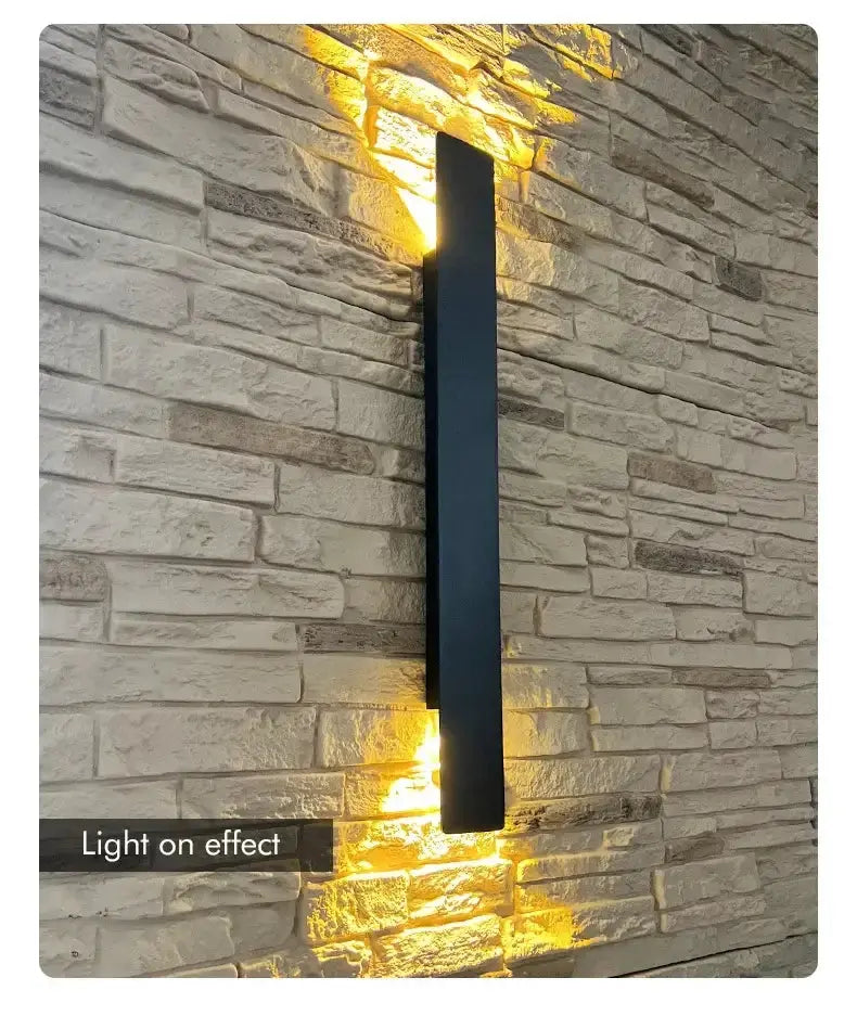 Aluminium LED wall lamp with light effect on a textured stone wall, showcasing modern outdoor lighting design.