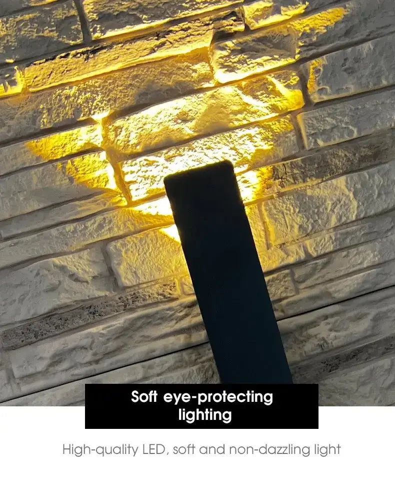 Applique murale LED en aluminium avec éclairage doux et protecteur, illuminant un mur en pierres.
