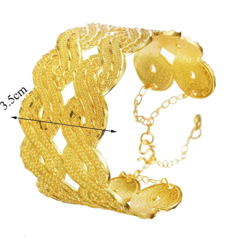 Wide gold-plated wave design cuff bracelet styled on a woman’s wrist with a traditional outfit.