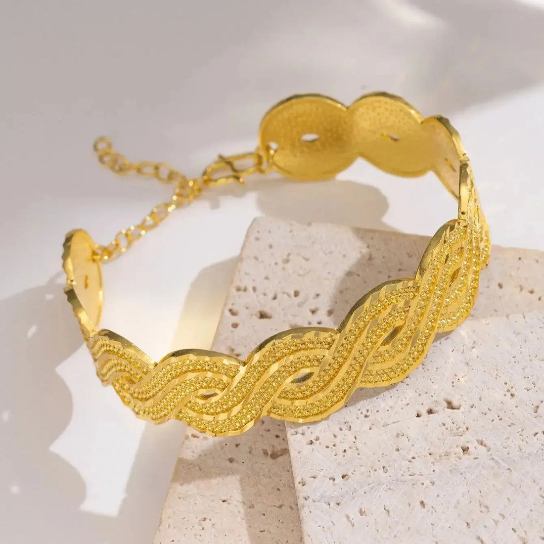 Wide gold-plated wave design cuff bracelet styled on a woman’s wrist with a traditional outfit.
