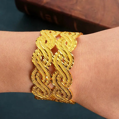 Wide gold-plated wave design cuff bracelet styled on a woman’s wrist with a traditional outfit.
