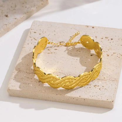 Wide gold-plated wave design cuff bracelet styled on a woman’s wrist with a traditional outfit.